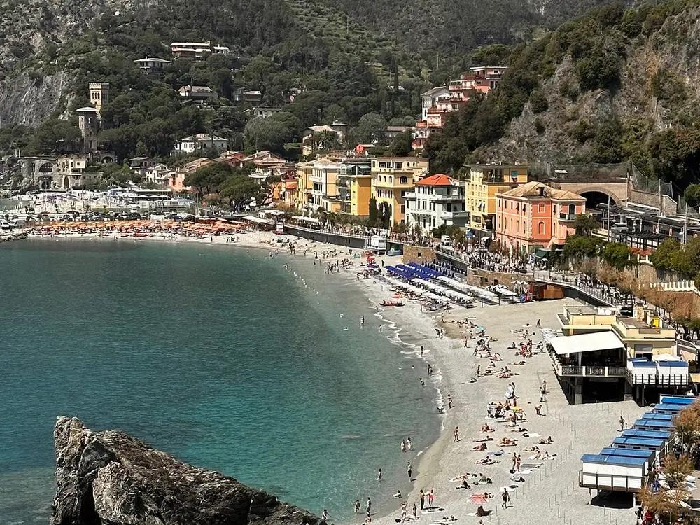 La curva della spiaggia di sabbia di Monterosso con ombrelloni e case color pastello alle spalle 