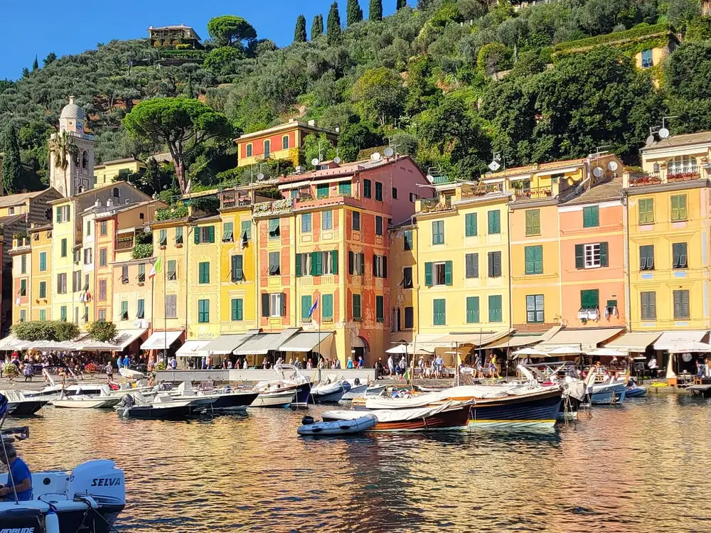 Hohe gelbe und orangefarbene Häuser an der Hafenpromenade von Portofino mit festgemachten Booten