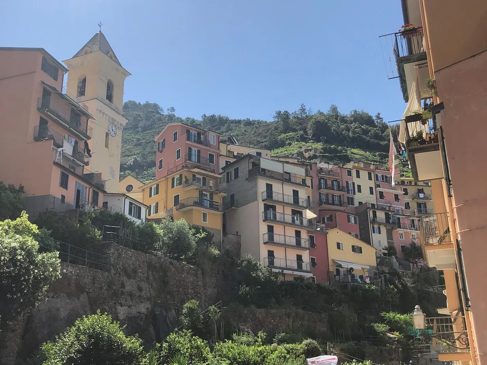 Bunte Häuser und ein Kirchturm, die den Hang über grünen Terrassen hinaufklettern